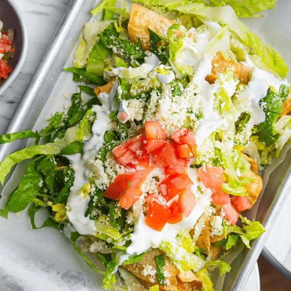 Crispy Mexican taquitos topped with fresh lettuce, diced tomatoes, sour cream, and crumbled cheese.