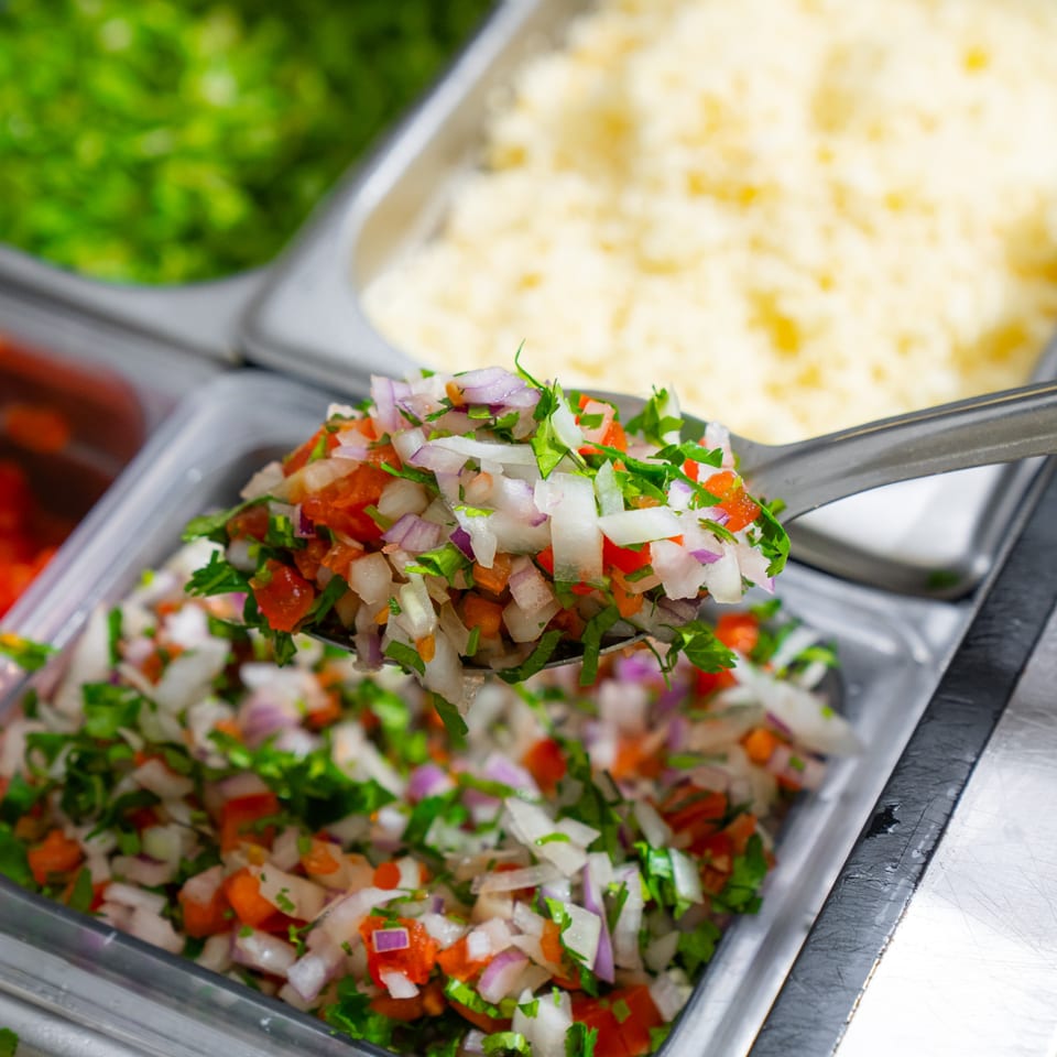 A metal spoon scoops fresh pico de gallo from a serving tray at Tacos & Bla Bla Bla.