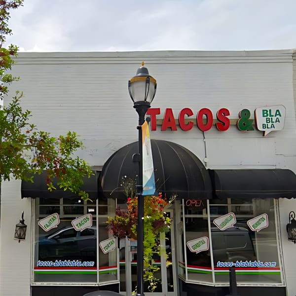 Exterior of Tacos & Bla Bla Bla restaurant with black awnings and menu items on windows.