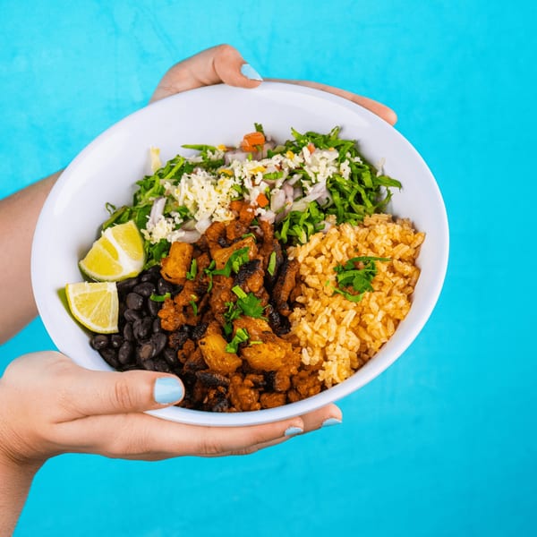 Hands holding a white bowl filled with Tacos & Bla Bla Bla's Mexican rice, black beans, and meat.
