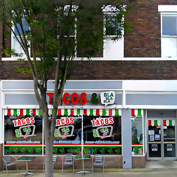The exterior of Tacos & Bla Bla Bla restaurant with red and green awnings and outdoor seating.