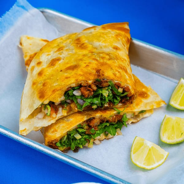Two golden-brown Tacos & Bla Bla Bla quesadillas, filled with meat, onions, and cilantro, served with lime wedges.