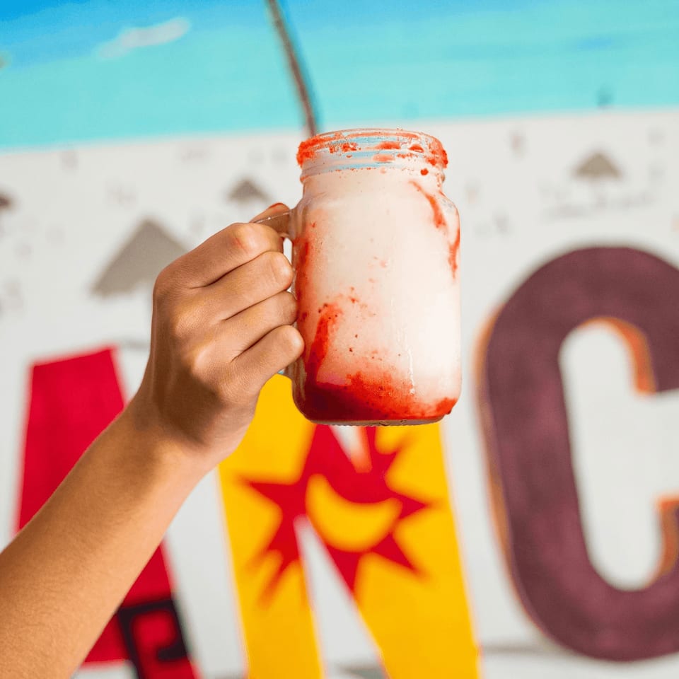 Hand holding a mason jar of strawberry horchata with a colorful mural in the background.