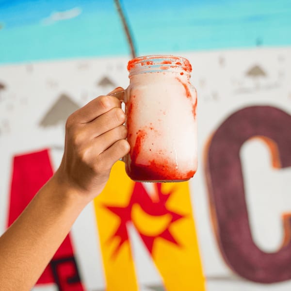 Hand holding a strawberry-swirled drink in a mason jar against a colorful mural.